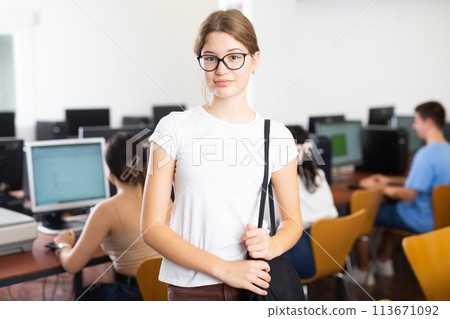 Portrait of smart female teenager in glasses standing in the middle of computer classroom Portrait of smart female teenager in glasses standing in the middle of computer classroom 113671092