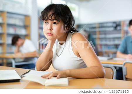 Asian teenager girl with a laptop studying in school library Asian teenager girl with a laptop studying in school library 113671115