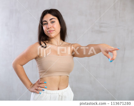 Young woman pointing aside standing against the wall 113671280
