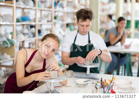 Pottery lesson - teenagers girl and guy intently create dishes from clay Pottery lesson - teenagers girl and guy intently create dishes from clay 113671327