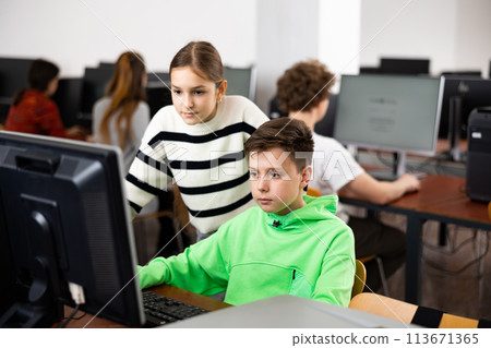 Teenager guy helps girl solve problem on computer in school class 113671365