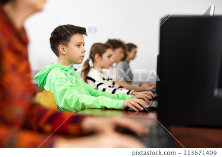Focused tween boy studying with classmates in computer lab Focused tween boy studying with classmates in computer lab 113671409