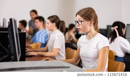 Positive female teenager in glasses learning computer science while she is using a PC in the computer classroom 113671418