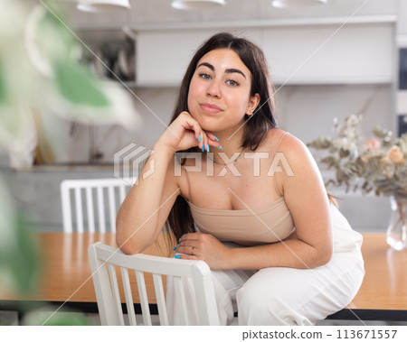 Smiling young woman posing sitting on kitchen table Smiling young woman posing sitting on kitchen table 113671557