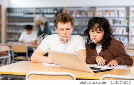 Focused young male and asian female students using laptop during studying in library 113671603