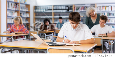 Focused teenager male student sitting at library desk, preparing for exam Focused teenager male student sitting at library desk, preparing for exam 113671622