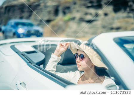 Woman looking at the ocean from the window of an open car 113673523