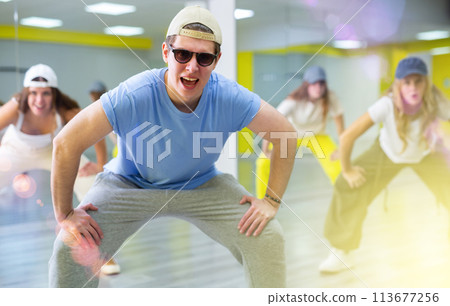 Group of young active tween dancers in casual wear performing dancing movement with legs wide apart in dance room 113677256