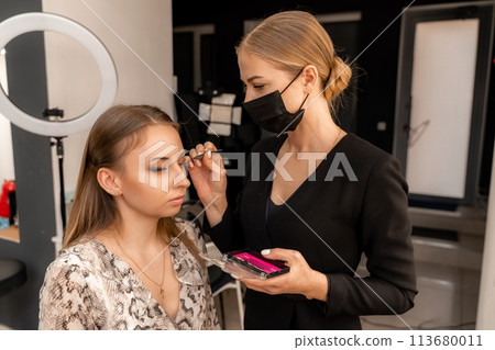 Makeup artist paints eyelashes to a woman in a beauty salon. Makeup artist paints eyelashes to a woman in a beauty salon. 113680011