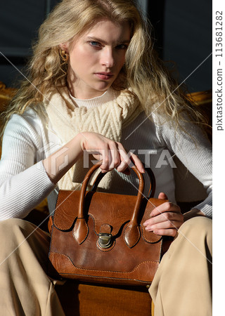 beautiful curly blond hair woman posing with a small brown leather bag on a vintage volor sofa beautiful curly blond hair woman posing with a small brown leather bag on a vintage volor sofa 113681282