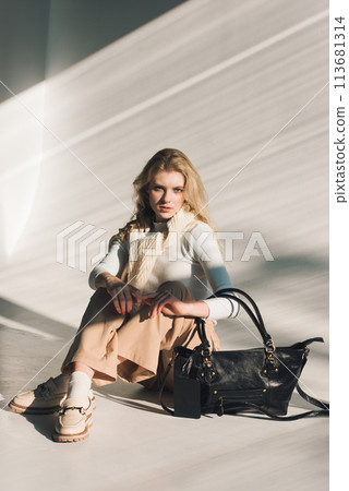 beautiful curly blond hair woman posing with a small shopper bag sitting on the floor 113681314