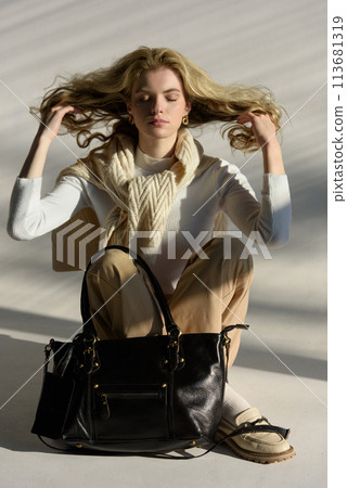 beautiful curly blond hair woman posing with a small shopper bag sitting on the floor 113681319