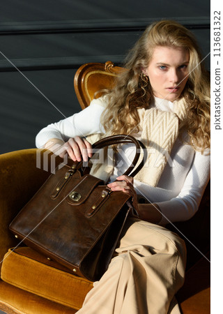 beautiful curly blond hair woman posing with a small shopper brown bag in a vintage chair beautiful curly blond hair woman posing with a small shopper brown bag in a vintage chair 113681322
