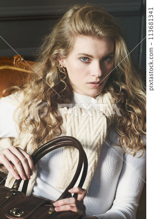 beautiful curly blond hair woman posing with a small shopper brown bag in a vintage chair 113681341