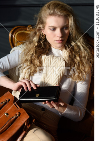 beautiful curly blond hair woman posing with a wallet and small shopper brown bag in a vintage chair beautiful curly blond hair woman posing with a wallet and small shopper brown bag in a vintage chair 113681349