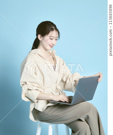 A young woman working on a PC against a blue background A young woman working on a PC against a blue background 113683896