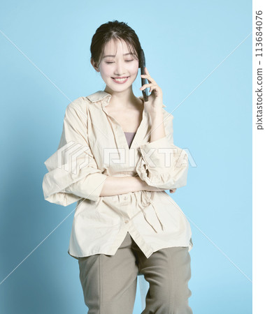 一位年輕女子拿著智慧型手機和一個包包,在藍色背景下拍照 一位年輕女子拿著智慧型手機和一個包包,在藍色背景下拍照 113684076