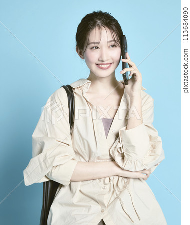 A young woman holding a smartphone and a bag photographed against a blue background A young woman holding a smartphone and a bag photographed against a blue background 113684090