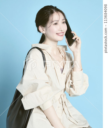 一位年輕女子拿著智慧型手機和一個包包，在藍色背景下拍照 113684098