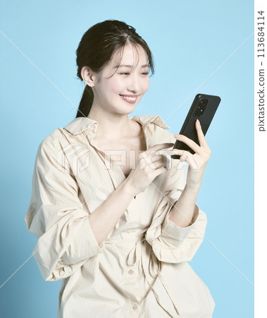 A young woman holding a smartphone and a bag photographed against a blue background 113684114