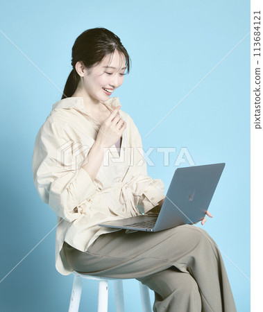 在藍色背景下拍攝的一位在電腦上工作的年輕女性 在藍色背景下拍攝的一位在電腦上工作的年輕女性 113684121