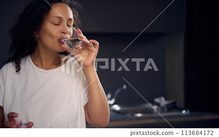 Close-up portrait of a pretty young woman drinking water in the morning, starting her day with a glass of refreshing water 113684172