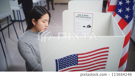 Asian female voter looking at camera standing in voting booth 113684246