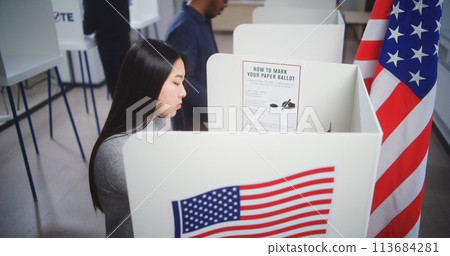 Asian woman comes to voting booth and fills out paper bulletin Asian woman comes to voting booth and fills out paper bulletin 113684281