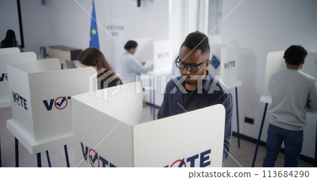 Diverse voters fill out ballots in voting booths during EU elections 113684290