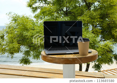 Laptop on table with coffee overlooking the sea Laptop on table with coffee overlooking the sea 113685580