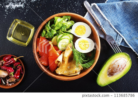 Delicious healthy brunch - boiled egg, smoked salmon, green salad and savory pancakes on a dark background, top view Delicious healthy brunch - boiled egg, smoked salmon, green salad and savory pancakes on a dark background, top view 113685786