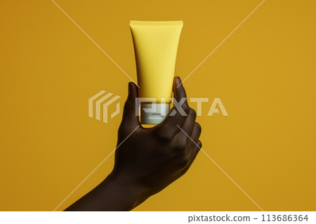 African American womans hand holds yellow tube on dark yellow background. Skin health care concept. African American womans hand holds yellow tube on dark yellow background. Skin health care concept. 113686364