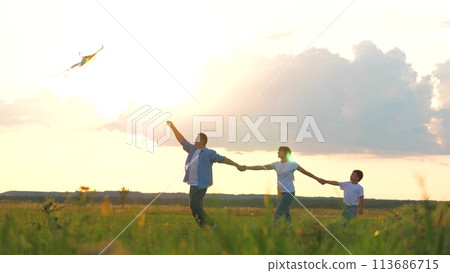 Family playing with flying kite holding hands at sunset grass wheat field outdoor leisure. Happy mother father and son relaxing enjoy freedom lifestyle weekend activity at meadow nature landscape Family playing with flying kite holding hands at sunset grass wheat field outdoor leisure. Happy mother father and son relaxing enjoy freedom lifestyle weekend activity at meadow nature landscape 113686715