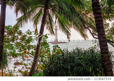 View of the lighthouse in the sea near the rocky shore through the palm trees. Sanya, China View of the lighthouse in the sea near the rocky shore through the palm trees. Sanya, China 113687354