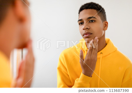 Black teen guy checking skin in mirror, looking thoughtful 113687390