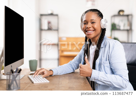 Positive black female student giving thumbs up at her desk with headphones 113687477