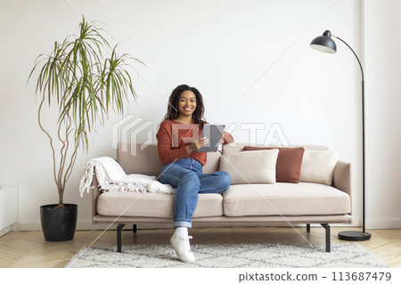Black Woman Sitting on Couch Using Tablet 113687479