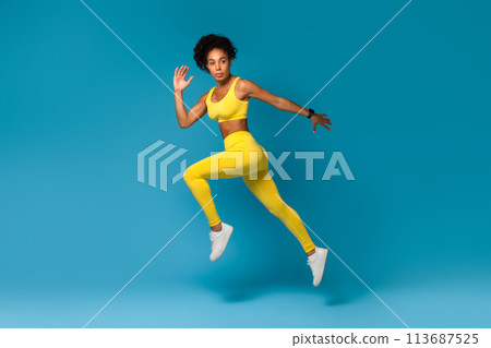 Athlete captured mid-air in yellow sportswear on blue background 113687525