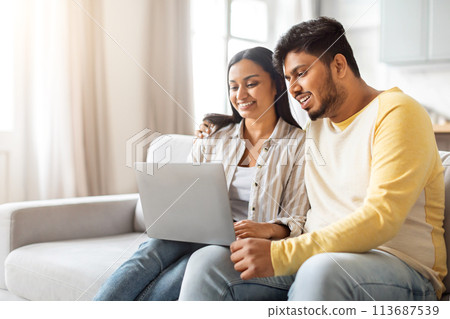 Indian Man and Woman Sitting on Couch Looking at Laptop 113687539