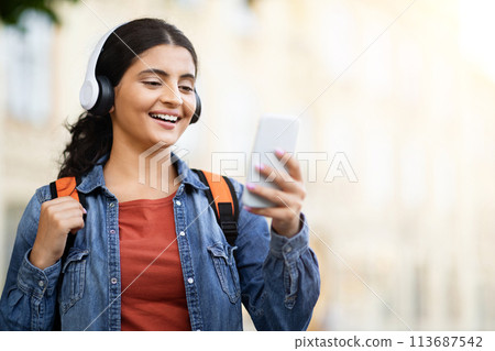 Indian student smiling with headphones, using phone Indian student smiling with headphones, using phone 113687542