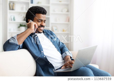Smiling Black Man Working From Home With Laptop and Smartphone 113687559