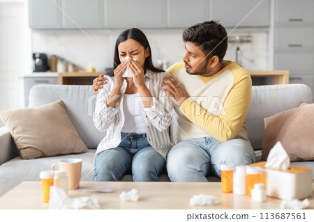 Indian Man Comforting Ill Woman Blowing Nose on Couch 113687561