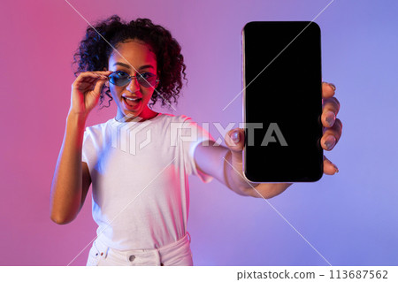 Joyful black woman with glasses showing phone with black screen 113687562