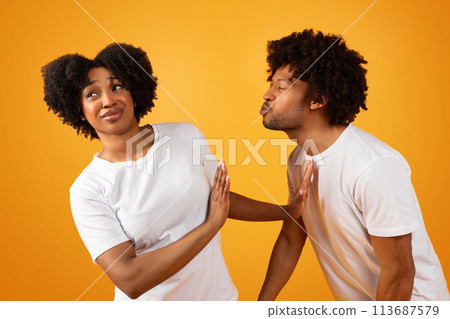 Disgusted black woman avoiding unwanted kiss from obsessed man 113687579