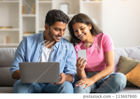 Cheerful indian couple using laptop and smartphone on sofa Cheerful indian couple using laptop and smartphone on sofa 113687600