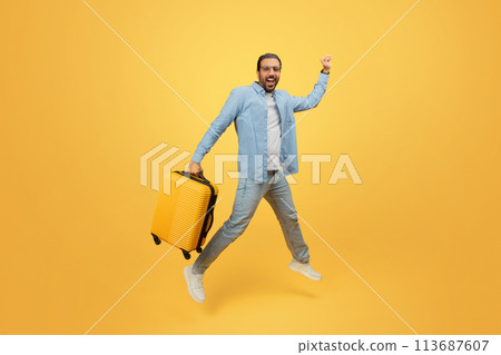 Man jumping with suitcase on yellow background Man jumping with suitcase on yellow background 113687607