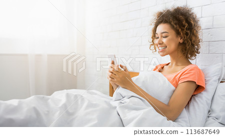 Happy girl texting on smartphone at home bedroom 113687649