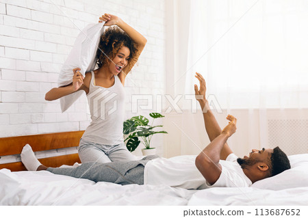 Playful pillow fight between smiling couple in bed Playful pillow fight between smiling couple in bed 113687652
