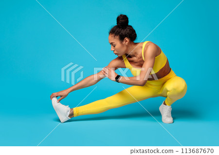 Focused athlete stretching in yellow outfit on blue background 113687670