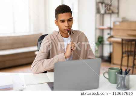 Thoughtful black teen guy studying with laptop at desk 113687680